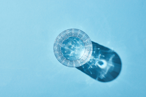 bovenaanzicht van glas met helder water op blauwe achtergrond met schaduw - Foto, afbeelding