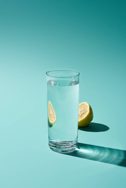 ターコイズ色の背景に淡水とレモンの半分と透明なガラス - 写真・画像