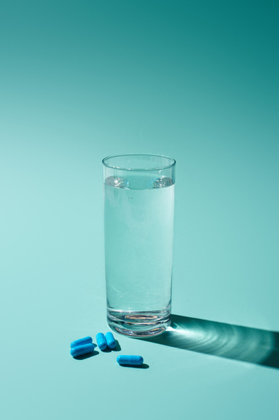 átlátszó üveg édesvízzel és kék tablettákkal, türkiz alapon - Fotó, kép