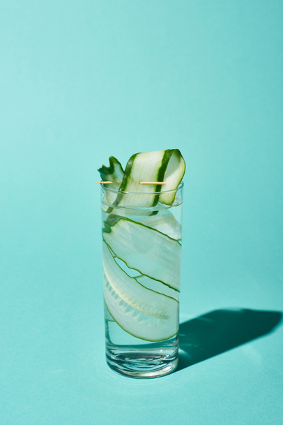 transparent glass with fresh water and cucumber slices on turquoise background - Фото, зображення