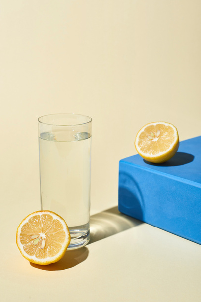 glass of water near lemon halves and blue cube on beige background - Фото, изображение