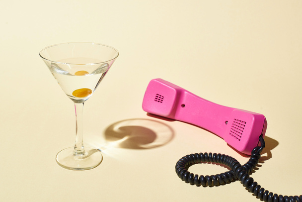 transparant glas met cocktail en Olive in de buurt van roze Vintage telefoon op beige achtergrond - Foto, afbeelding