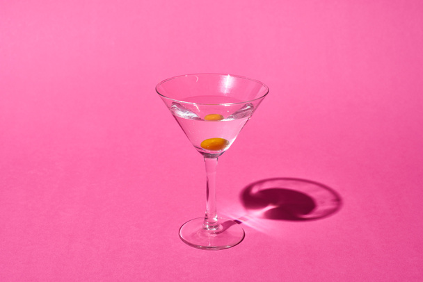 transparent glass with cocktail and olive on pink background - Fotoğraf, Görsel