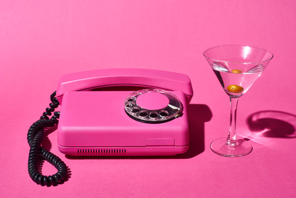 transparent glass with cocktail and olive near vintage dial phone on pink background - Фото, зображення