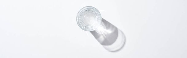 Κορυφαία όψη του διαφανούς γυαλιού με νερό σε λευκή επιφάνεια με σκιά, πανοραμική βολή - Φωτογραφία, εικόνα