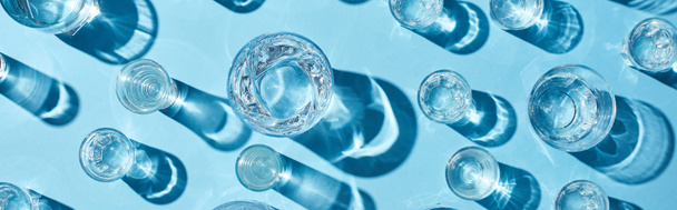 top view of transparent glasses with clear water and shadows on blue background, panoramic shot - Photo, Image