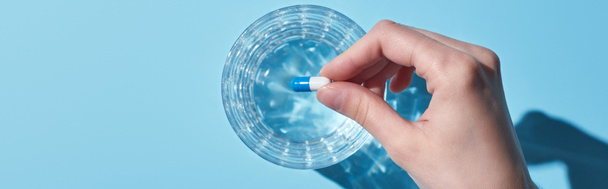 vista recortada de la mujer poner píldora en vidrio con agua sobre fondo azul, tiro panorámico
 - Foto, imagen