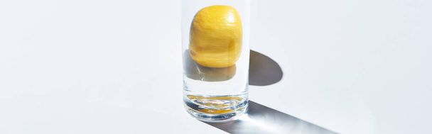 panoramic shot of transparent glass with water and whole lemon on white background  - Valokuva, kuva