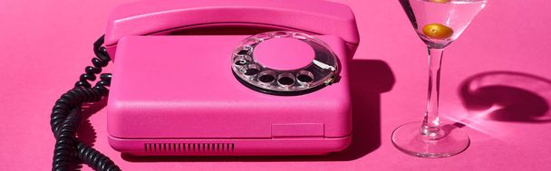 panoramic shot of transparent glass with cocktail and olive near vintage dial phone on pink background - Foto, immagini