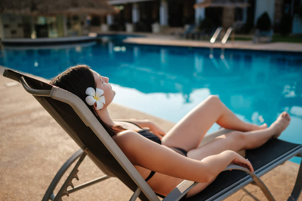 Φωτογραφία μιας νεαρής γυναίκας που χαλαρώνει στην πολυτελή πισίνα. Καλοκαιρινές διακοπές. - Φωτογραφία, εικόνα
