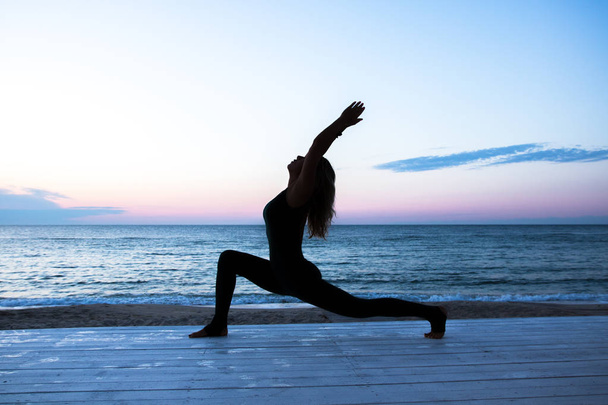 unrecognizable woman with beautiful body doing yoga at sunrise on the sea, silhouette of yoga poses - Photo, image