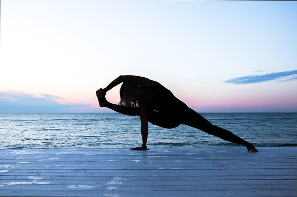 donna irriconoscibile che fa yoga all'alba sul mare, silhouette di pose yoga
 - Foto, immagini