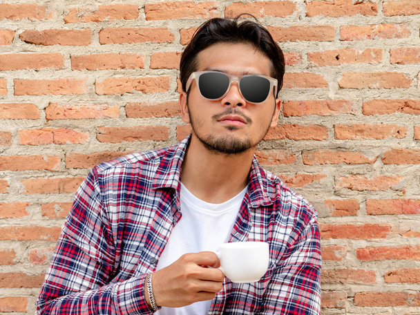 Tuğla duvara karşı kahve fincanı tutan genç adam. - Fotoğraf, Görsel