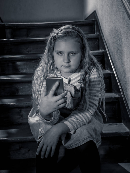 Грустная депрессивная молодая девушка, жертва кибериздевательств с помощью мобильного смартфона, сидящая на лестнице, чувствующая себя одинокой, несчастной, безнадежной и оскорбленной. Над ребенком издевались и преследовали его текстовые сообщения онлайн-преследователя.
. - Фото, изображение