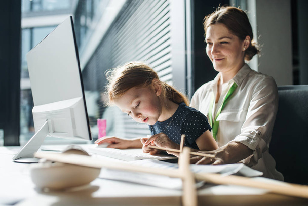 A businesswoman with small daughter sitting in an office, working. - Valokuva, kuva
