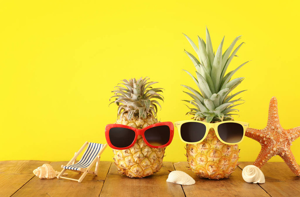 Ripe couple pineapple in stylish sunglasses over wooden table or deck, relaxing. Tropical summer vacation concept - Foto, Imagem