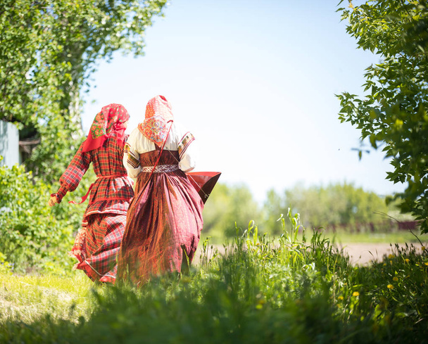 Geleneksel Rus kıyafetleri içinde iki genç kadın ağaçların arasındaki alanda duruyor - Fotoğraf, Görsel