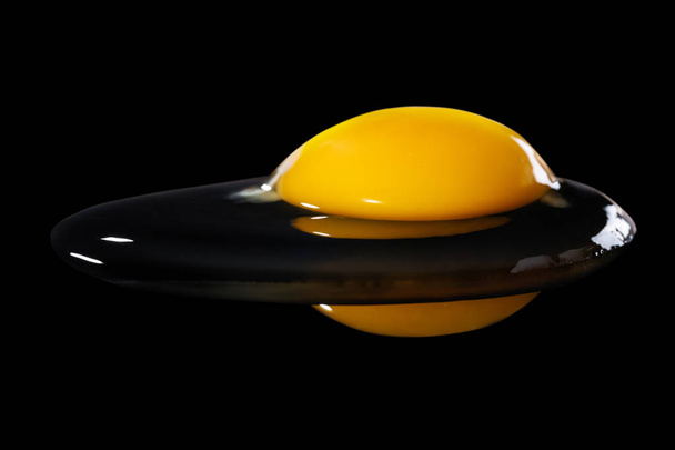 Raw the broken egg on a black background - Foto, afbeelding