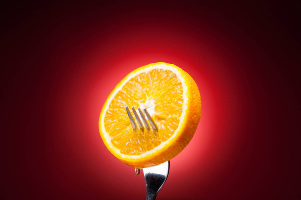 orange slice on fork on red background - Фото, изображение