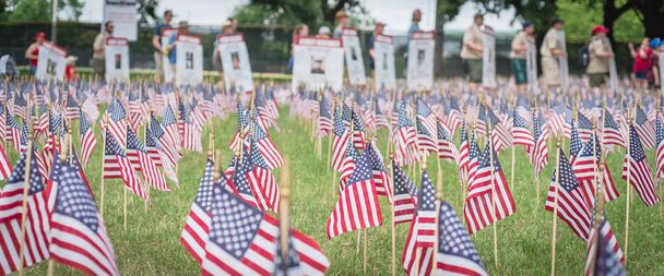 Césped panorámico Banderas estadounidenses con fila borrosa de personas llevan desfile de pancartas de soldados caídos
 - Foto, Imagen