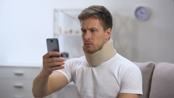 Man in foam cervical collar reading message on cellphone, feeling pain in neck - Кадри, відео