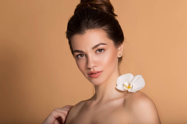 Closeup portrait of young beautiful girl with flawless skin with white orchid flower on her shoulder. Skin care, beauty and cosmetics concept. - Fotografie, Obrázek