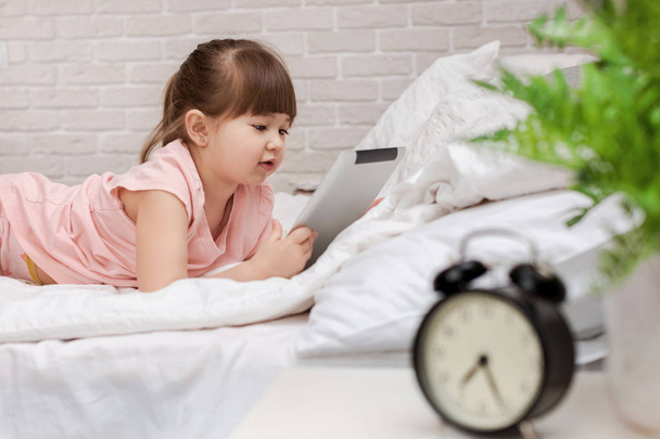 little child girl lies in bed uses digital tablet. - Φωτογραφία, εικόνα