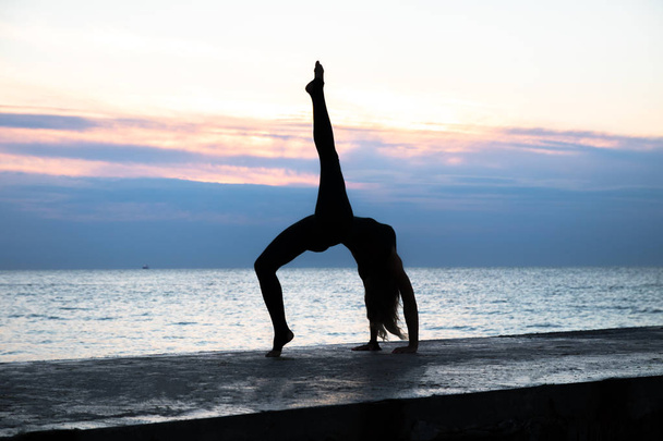 unrecognizable senoir woman with beautiful body profissiionally doing yoga at sunrise on the sea, silhouette of yoga poses - Photo, Image