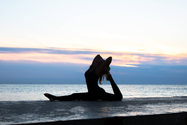 senoir méconnaissable femme avec beau corps faisant des splits de yoga au lever du soleil sur la mer, silhouette de poses de yoga
 - Photo, image
