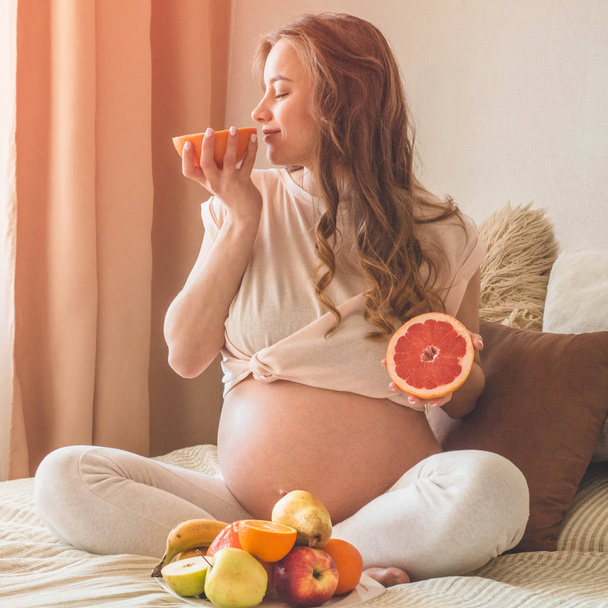 Вагітність і здорове органічне харчування. Вагітність і грейпфрут. Вагітна жінка насолоджується свіжими фруктами в ліжку, вільний простір
. - Фото, зображення