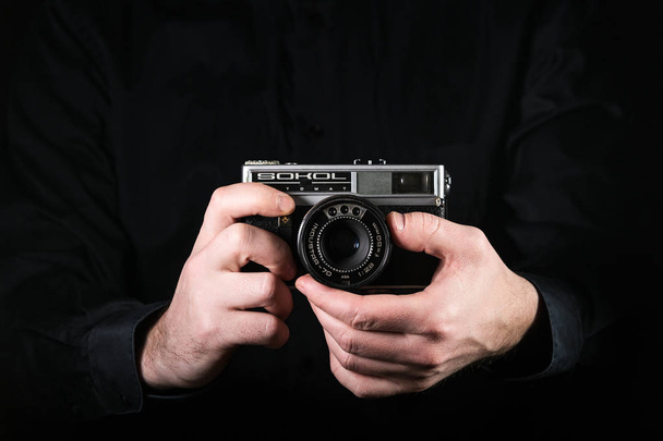 Chisinau, Repubblica di Moldova - 12 marzo 2019: fotografo uomo con una fotocamera in mano. Processo di ripresa. Macchina fotografica retrò russa Sokol
. - Foto, immagini