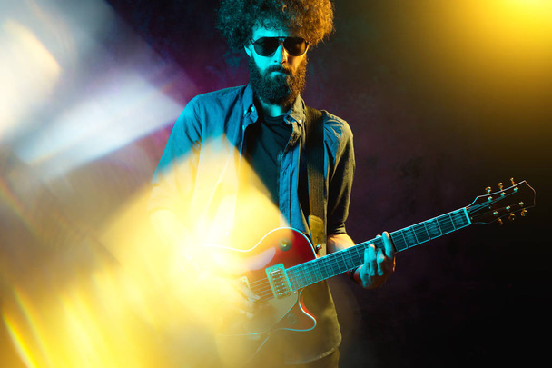 Close-up photo of hipster man with red guitar in neon lights. Rock musician is playing electrical guitar. - Foto, immagini