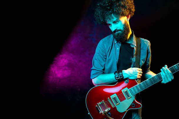 Close-up foto van hipster man met rode gitaar in neonlichten. Rock muzikant speelt elektrische gitaar. - Foto, afbeelding