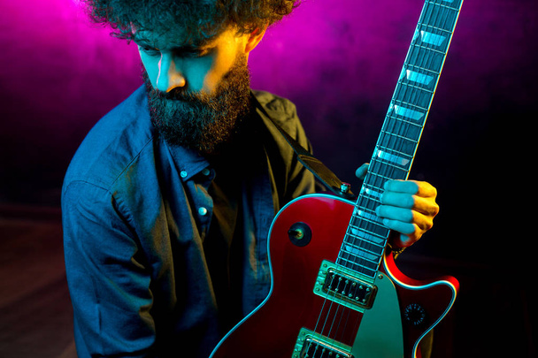 Close-up photo of hipster man with red guitar in neon lights. Rock musician is playing electrical guitar. - Fotografie, Obrázek