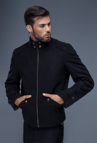 knappe man met een trendy kapsel in zwarte jas, zwart shirt - Foto, afbeelding