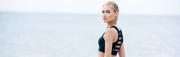 panoramic shot of attractive blonde young woman in sportswear looking at camera near sea  - Photo, image