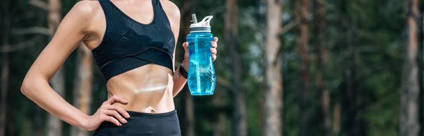 panoramic shot of woman holding sport bottle while standing with hand on hip  - Foto, imagen
