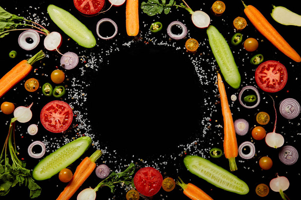 Draufsicht auf frische Gemüsescheiben mit Salz mit leerem Rundrahmen isoliert auf schwarz  - Foto, Bild