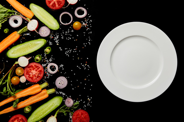вид зверху порожня кругла тарілка біля овочевих скибочок ізольовано на чорному
 - Фото, зображення