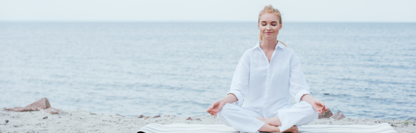 Panoramaaufnahme einer friedlichen blonden jungen Frau mit geschlossenen Augen, die in Flussnähe Yoga praktiziert  - Foto, Bild
