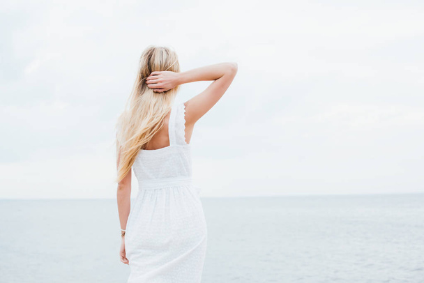 Rückansicht einer jungen Frau, die am Meer steht und Haare berührt  - Foto, Bild