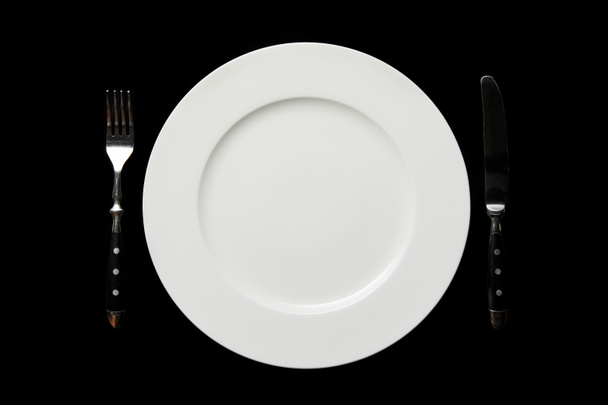 top view of white empty round plate and knife with fork isolated on black - Photo, Image