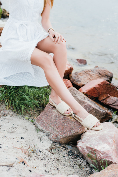 vista recortada de mujer joven en vestido blanco sentado en piedras cerca del mar
  - Foto, imagen