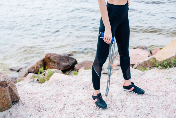 cropped view of young sportswoman standing near sea and holding jump rope  - Photo, image