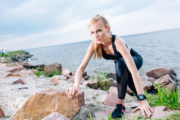 overhead view of athletic blonde sportswoman climbing near stones and sea - Fotografie, Obrázek