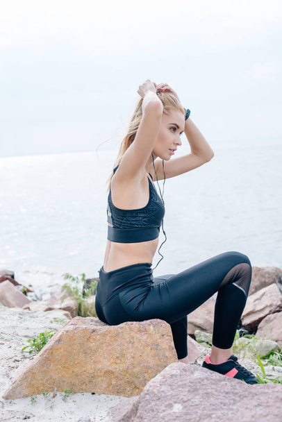attractive athletic girl touching hair while listening music in earphones near sea  - 写真・画像