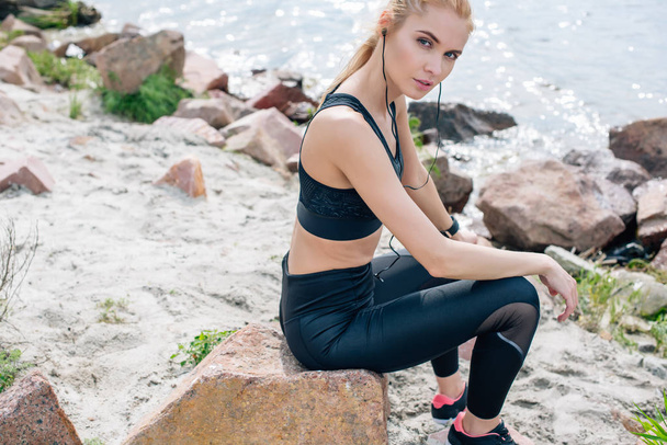 athletic young woman sitting on stone and listening music in earphones  - Foto, immagini