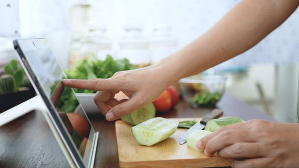 Ασιατικές γυναίκα χρησιμοποιούν διαφάνειες δάχτυλο στην οθόνη του tablet προετοιμάσει τα συστατικά για το μαγείρεμα ακολουθήστε μαγείρεμα online βίντεο κλιπ στην ιστοσελίδα. περιεχόμενο μαγειρικής στην τεχνολογία Internet για την έννοια του σύγχρονου τρόπου ζωής - Φωτογραφία, εικόνα