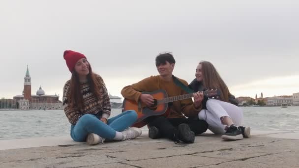 Un grupo de jóvenes amigos sentados en el borde del muelle y cantando canciones de la guitarra
 - Imágenes, Vídeo