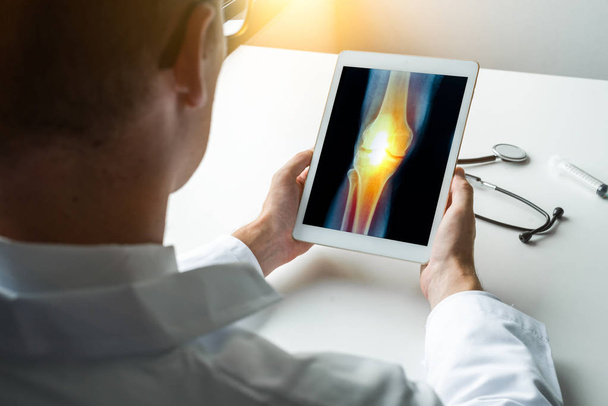 Arzt hält ein digitales Tablet mit Röntgenbild des Schmerzes am Knie. Frontansicht - Foto, Bild